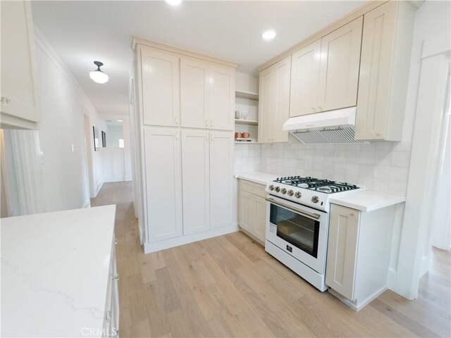 kitchen featuring white range with gas stovetop, under cabinet range hood, light wood-style flooring, backsplash, and open shelves