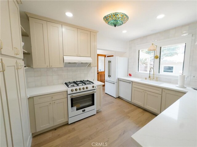kitchen featuring white appliances, a sink, under cabinet range hood, backsplash, and light wood-style flooring