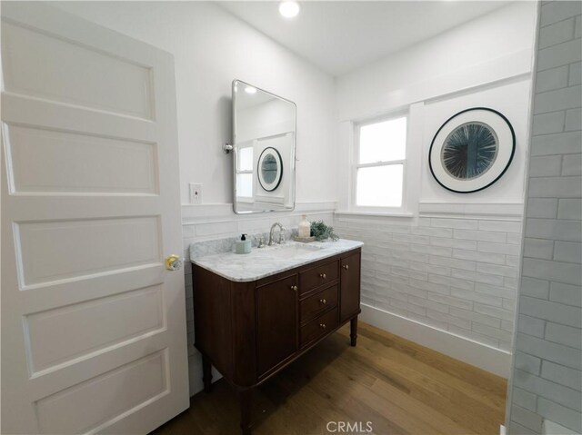 bathroom with wood finished floors, vanity, wainscoting, and tile walls