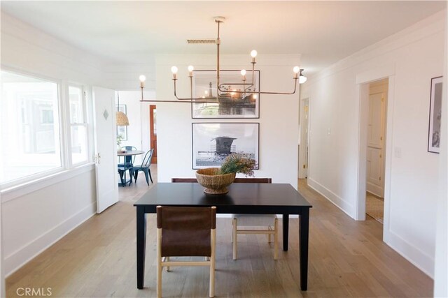 dining area with a chandelier, light wood finished floors, baseboards, and ornamental molding
