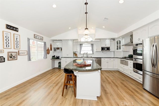 1417 E Abbottson St, Carson, CA 90746 - kitchen featuring appliances with stainless steel finishes, wall chimney range hood, lofted ceiling, a kitchen breakfast bar, and glass insert cabinets