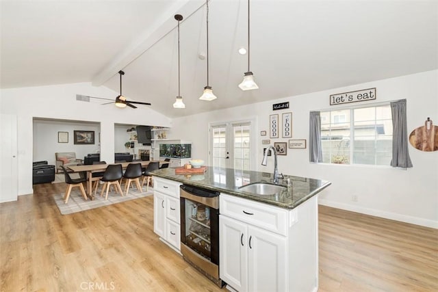 kitchen featuring a sink, beverage cooler, a center island, white cabinets, and dark stone countertops