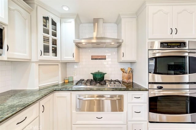 kitchen with wall chimney exhaust hood, stainless steel appliances, a warming drawer, and white cabinetry