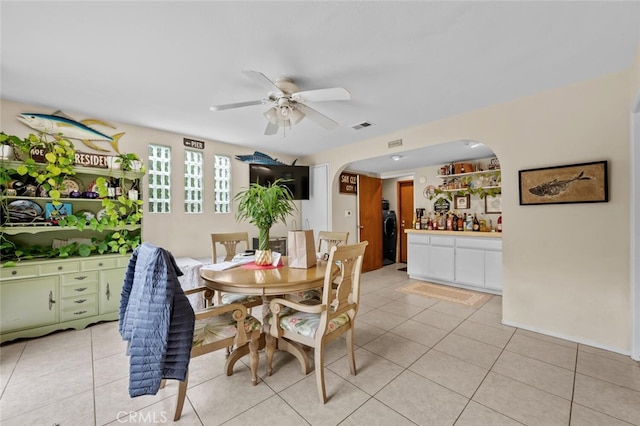 dining space featuring arched walkways, a ceiling fan, light tile patterned floors, and washer / dryer