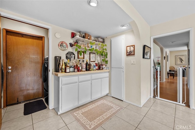 indoor dry bar featuring arched walkways, light tile patterned floors, and baseboards