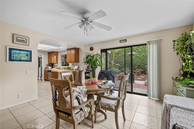 dining area with arched walkways, light tile patterned floors, ceiling fan, and baseboards