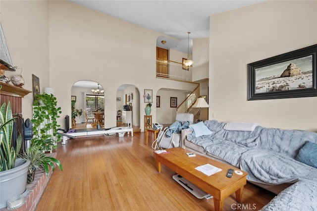 living room featuring arched walkways, a chandelier, wood finished floors, and a towering ceiling