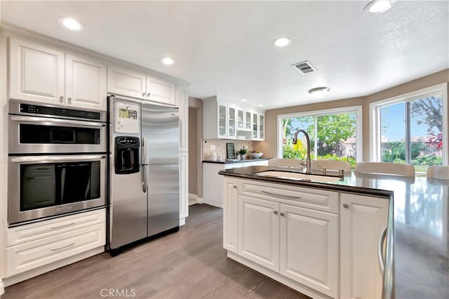 kitchen with stainless steel appliances, a sink, white cabinets, dark countertops, and recessed lighting