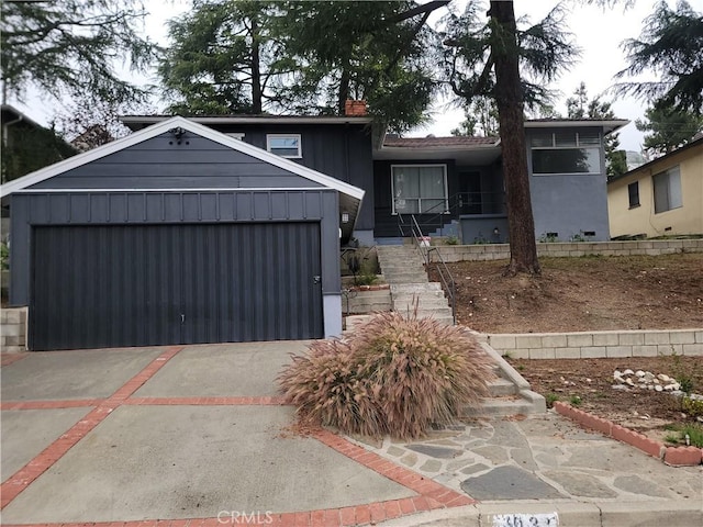 split level home with an attached garage, driveway, stairway, and board and batten siding