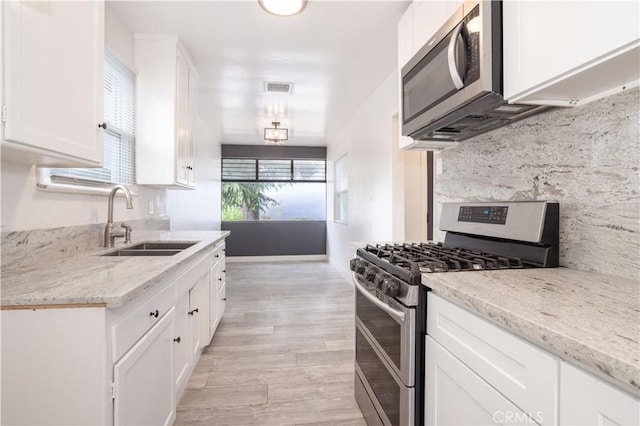 kitchen featuring stainless steel appliances, a sink, white cabinets, light wood-type flooring, and light stone counters
