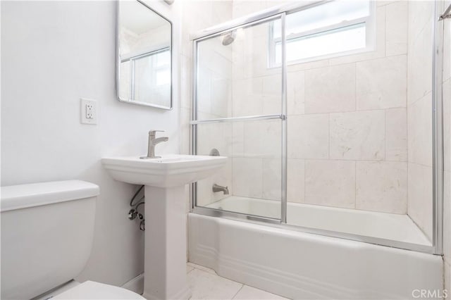 bathroom featuring toilet and shower / bath combination with glass door