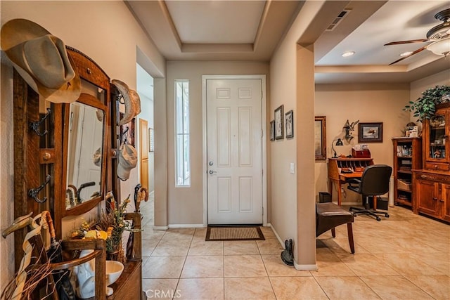 entrance foyer featuring a tray ceiling, ceiling fan, light tile patterned floors, and baseboards