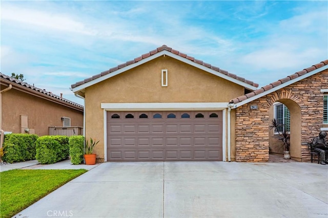 view of front of home with driveway, stone siding, stucco siding, a tile roof, and a garage