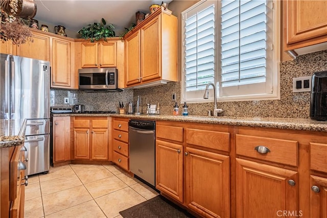 kitchen with stainless steel appliances, a sink, light tile patterned flooring, decorative backsplash, and light stone counters