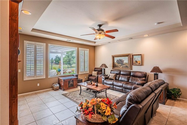 living area featuring a tray ceiling, light tile patterned floors, and ceiling fan