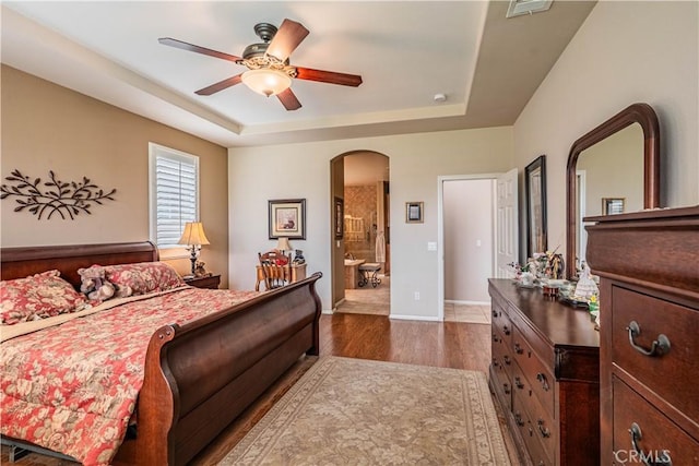 bedroom with arched walkways, a raised ceiling, dark wood-style floors, baseboards, and ceiling fan