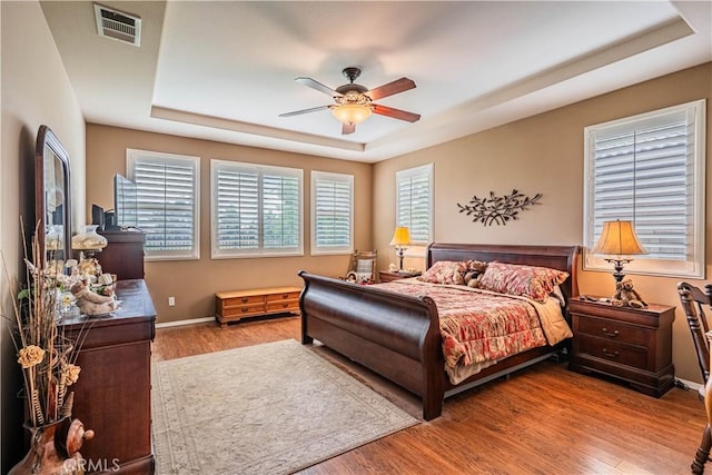 bedroom with a raised ceiling, wood finished floors, baseboards, and ceiling fan