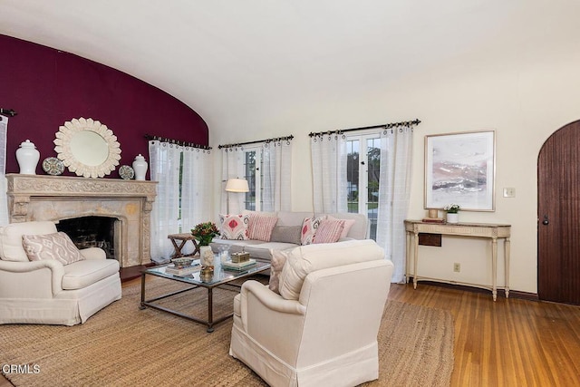 living area with wood finished floors, lofted ceiling, baseboards, and a high end fireplace