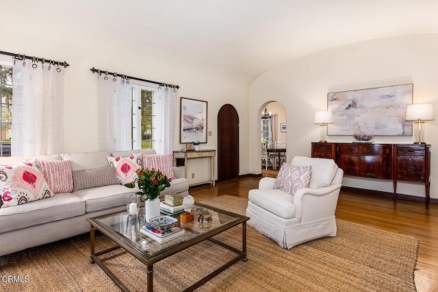 living area with wood finished floors, arched walkways, vaulted ceiling, and healthy amount of natural light