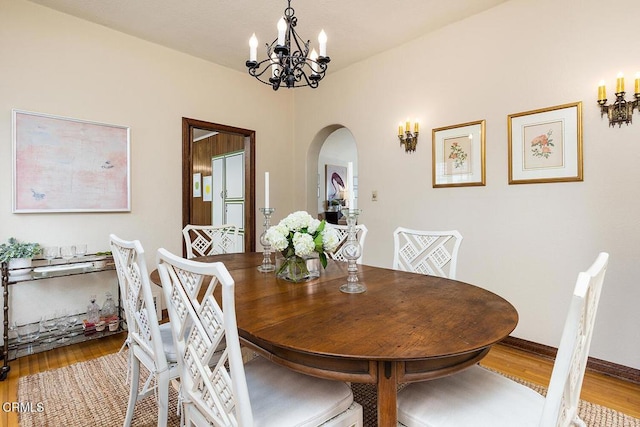 dining area with arched walkways, a chandelier, wood finished floors, and baseboards