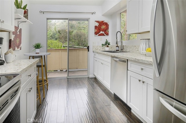 kitchen with stainless steel appliances, a sink, white cabinets, light stone counters, and dark wood finished floors