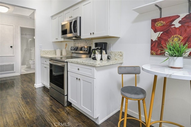 kitchen with stainless steel appliances, dark wood-style floors, white cabinets, and light stone counters
