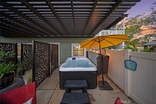 patio terrace at dusk with a hot tub, a pergola, and fence