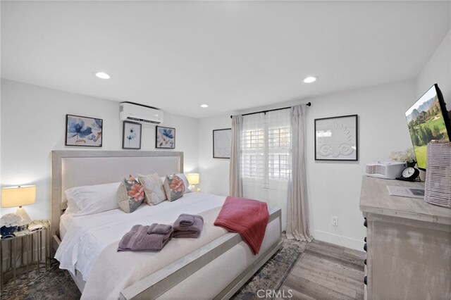 bedroom featuring a wall mounted AC, wood finished floors, recessed lighting, and baseboards