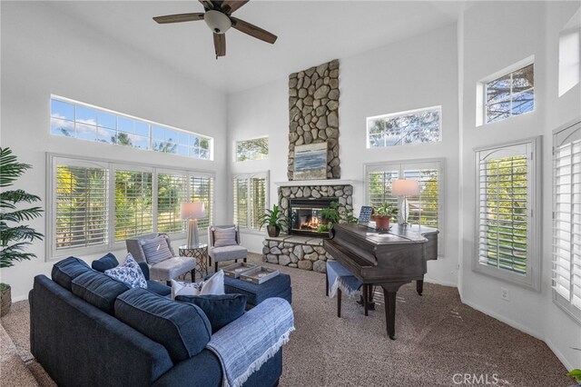 carpeted living room with a high ceiling, a ceiling fan, healthy amount of natural light, a stone fireplace, and baseboards