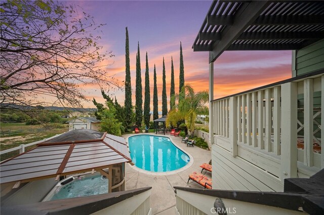 pool at dusk featuring a hot tub, a patio, an outdoor pool, and a pergola