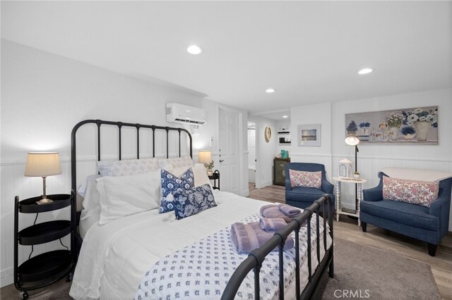 bedroom with a wall unit AC, wood finished floors, recessed lighting, and baseboards