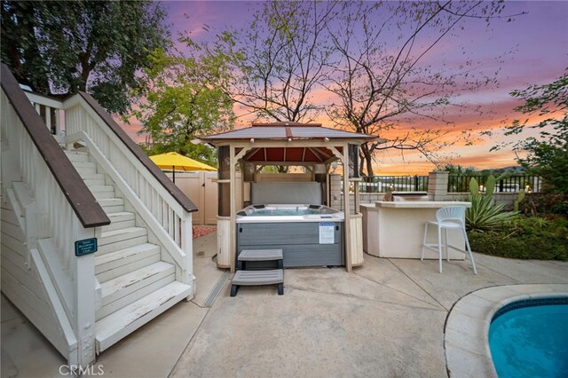 patio terrace at dusk featuring a hot tub, a gazebo, a fenced backyard, and stairway