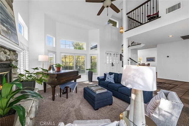 living room with stairway, a high ceiling, a ceiling fan, healthy amount of natural light, and a fireplace