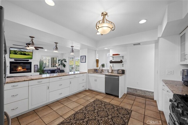kitchen with stainless steel dishwasher, gas stove, a fireplace, white cabinets, and a ceiling fan