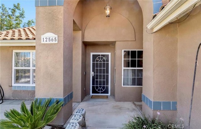 view of exterior entry with stucco siding and a patio