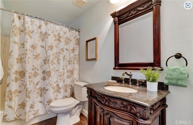 full bathroom featuring toilet, vanity, a textured wall, and wood finished floors