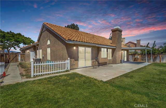 back of house at dusk with stucco siding, a chimney, a patio, and a tile roof
