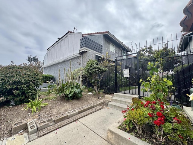 view of side of home featuring fence, a tiled roof, and stucco siding