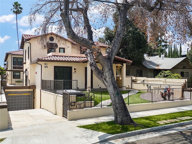 mediterranean / spanish-style home featuring a tile roof, stucco siding, a fenced front yard, and a gate