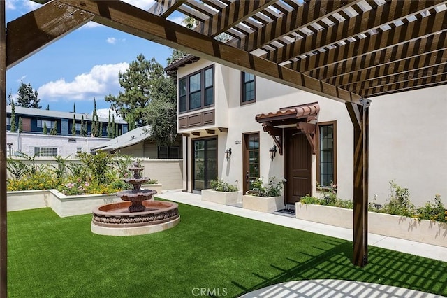 rear view of property featuring stucco siding, a yard, and a pergola