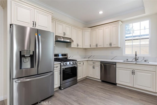 kitchen featuring stainless steel appliances, a sink, under cabinet range hood, crown molding, and light wood finished floors