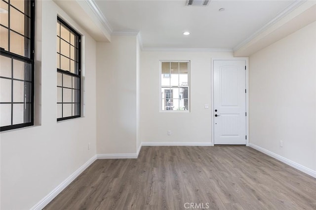 empty room with wood finished floors, crown molding, baseboards, and recessed lighting