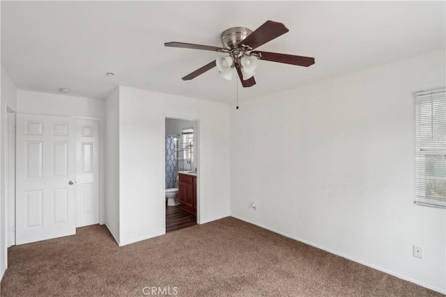 unfurnished bedroom with dark carpet, ensuite bathroom, and ceiling fan