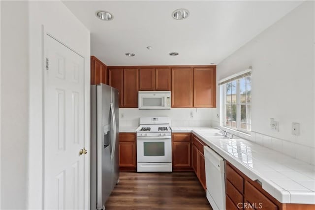 kitchen with white appliances, dark wood-type flooring, tile counters, recessed lighting, and brown cabinets