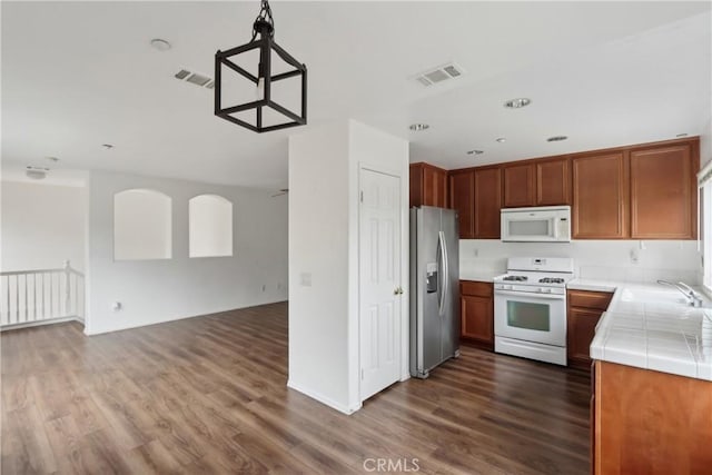 kitchen featuring white appliances, tile counters, a sink, open floor plan, and dark wood-type flooring