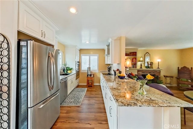 kitchen with appliances with stainless steel finishes, wood finished floors, white cabinets, a peninsula, and a sink