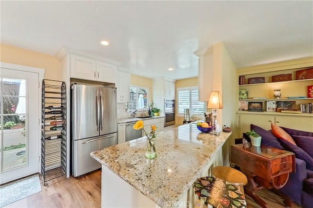 kitchen featuring appliances with stainless steel finishes, a sink, white cabinetry, light stone counters, and a peninsula