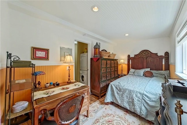 bedroom with stacked washing machine and dryer, wainscoting, light wood-style floors, wood walls, and recessed lighting