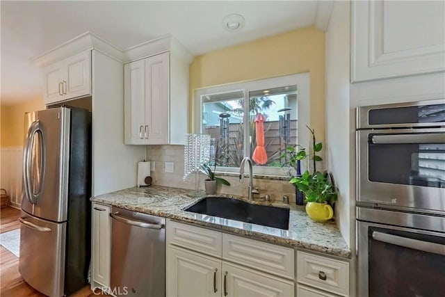 kitchen with appliances with stainless steel finishes, a sink, white cabinetry, and decorative backsplash