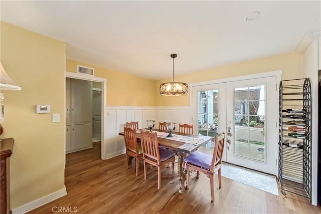 dining area featuring wood finished floors, french doors, a chandelier, and wainscoting